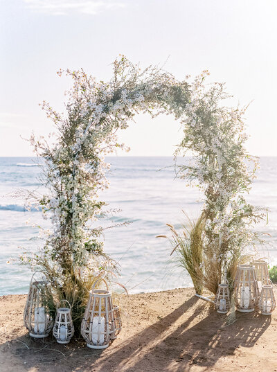 Wedding floral arch beside the ocean captured in heirloom fine art style, perfect for luxury estate and destination weddings.
