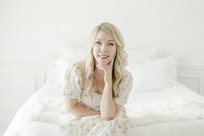 Photographer in white dress sitting on bed