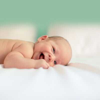 A baby smiling and laying down on a sheet