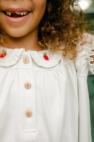 A little girl wearing a white dress with embroidered red apples back to school