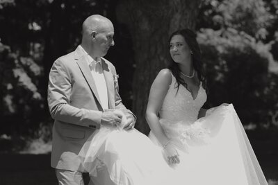 black and white wedding portrait of groom carrying brides  train