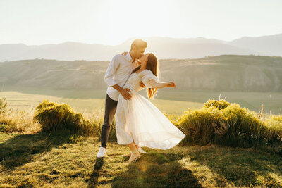 man and woman kissing while standing outside with mountains in the distance