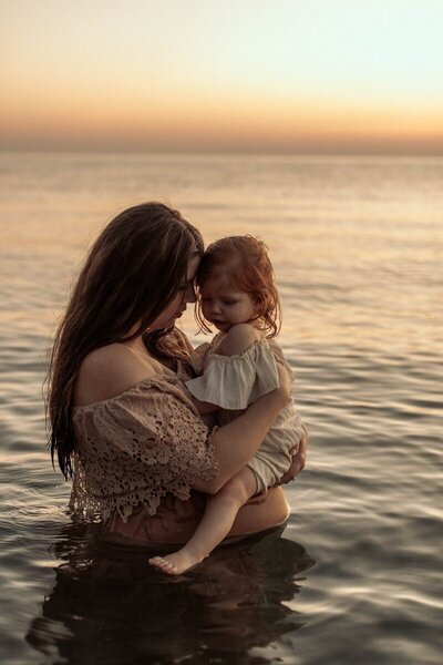 Mother holding daughter in golden hour water session captured by a Michigan photographer