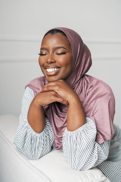 Woman wearing purple hijab smiling with eyes closed and laughing