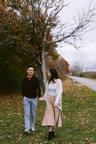 The couple walking hand in hand along a tree-lined path in autumn