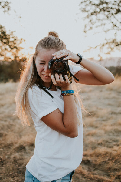 Noël Brower stands in field at sunset while looking through her camera at the photographer