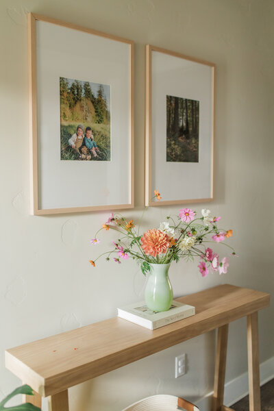 Hallway console table with a vase of colorful flowers and two framed pictures