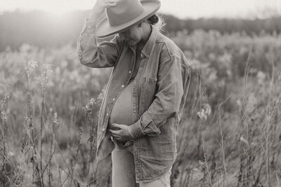 Expecting mother cradles her pregnant belly while standing in Minnesota meadow