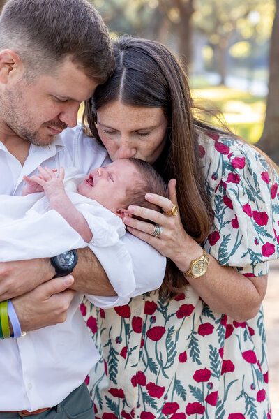 mom kisses baby's head while dad holds her