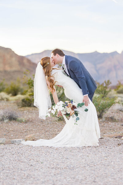 Groom in a blue suit dipping Red headed bride  and kissing her in front of Red Rock Canyon in Las Vegas, Nevada