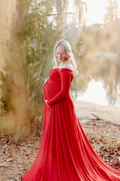 Pregnant mother poses in luxury red maternity gown at The Resting Place Venue in Flora Mississippi.