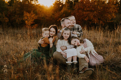 Family of 6 sitting in the tall grass cuddled together laughing and hugging.