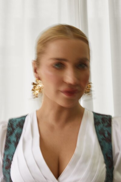 Frau in traditionellem Dirndl von Monaco Spatzl mit blauer Schulterpartie, kombiniert mit goldenen Ohrringen. Das Outfit kombiniert klassische Trachtenmode mit modernen Akzenten und eleganten Accessoires für einen stilvollen Auftritt.