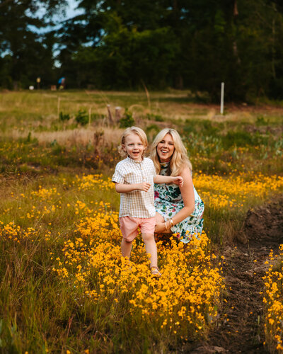 Mother squats down and smiles at her playful toddler while he runs through a Georgia wildflower field.