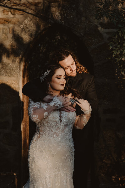A newlywed couple standing on in front of the other hugging 