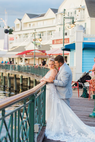 Groom cuddling with his Disney bride in front of the Epcot lagoon by Sea Breeze Point at Disney World.