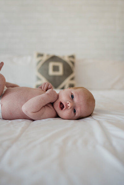 Close up of baby laying in crib on a green sheet in just a diaper with sun coming through casting shadows during an in home newborn session