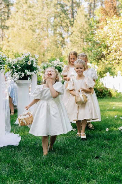 Flower girls walk down the aisle at the Belle Gardens wedding venue in their white satin dresses throwing flower petals before the bride walks down the aisle