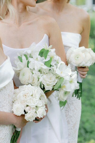 Wedding reception in a text, long rectangle tabled with a white table cloth, wood cushioned chairs, white bouquets hanging above , and at the end of the table there are white flowers and greenery on the floor