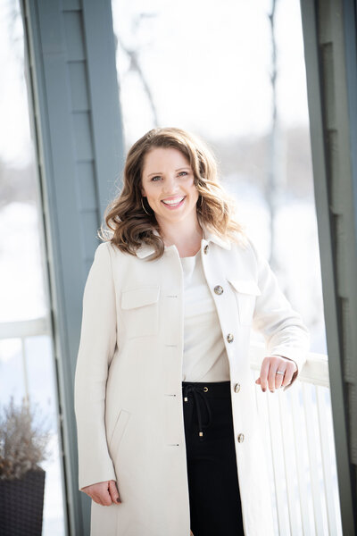 A white woman wearing a white coat, white blouse, and black pants, smiling at the viewer