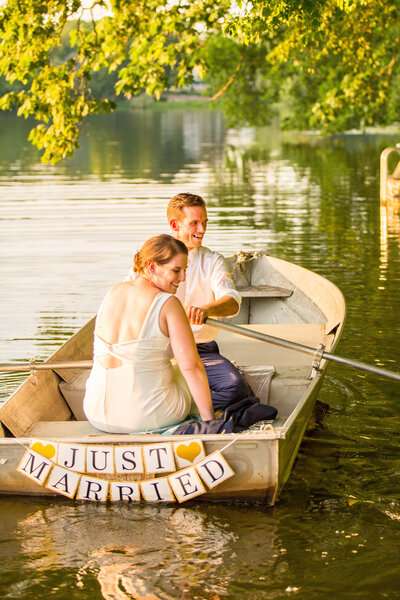 Bride and groom laugh as they sit in  a rowboat.