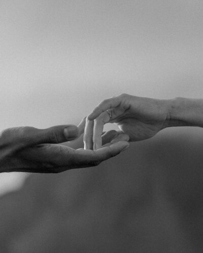 Romantic black and white photo of two hands softly reaching toward each other — a poetic moment captured during an intimate elopement.