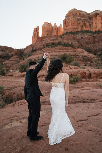 Bride and groom dancing on red rock terrain during their Sedona elopement at Cathedral Rock, with sandstone cliffs in the background.