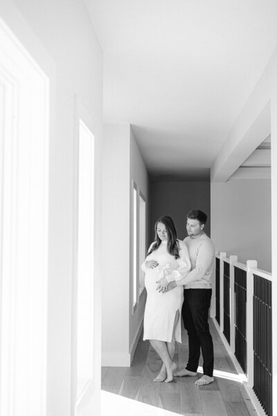 black and white of a maternity session of a couple holding mom's pregnant belly in a hallway