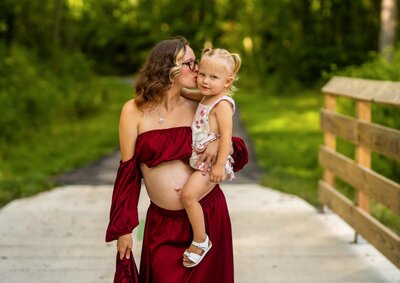 pregnant mom in white crop top and jeams holding a white and yellow boquet leaning on the wall with her husband as he gazes at her