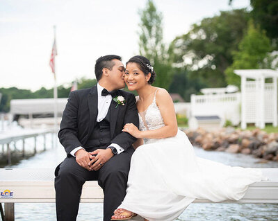 groom kisses bride's cheek on lakeside dock