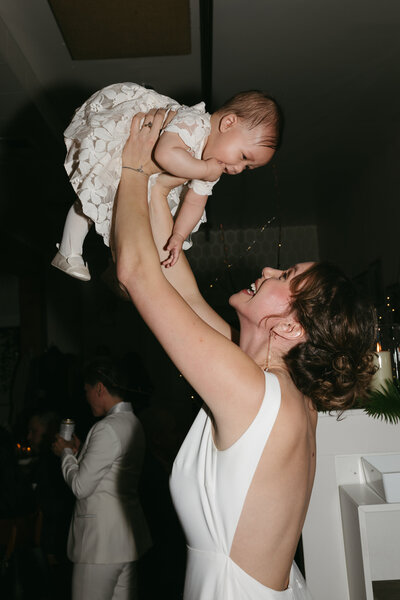 A bride holds her baby in the air at her intimate wedding.