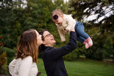 LGBTQ+ couple raising baby girl into the air in a Warren MI park