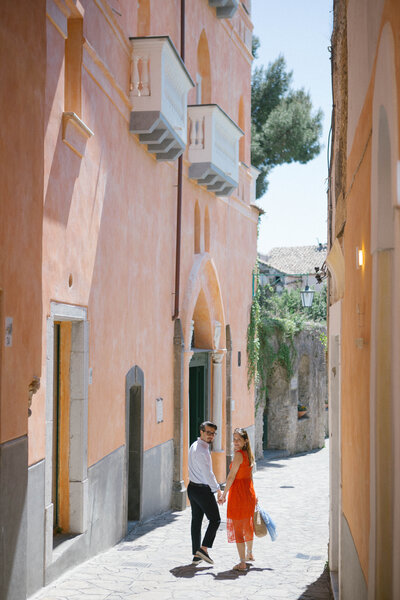 Stylish couple walking through colorful Italian alleyway – destination portrait session in sunlit coastal village