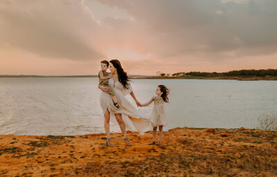 A mom and her two kids are standing near the waters edge at Murrell Park while the wind blows their hair.