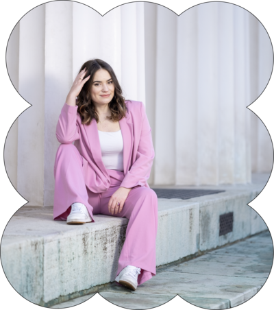 Shapely Studio founder sitting on the stairs, wearing a full pink suit