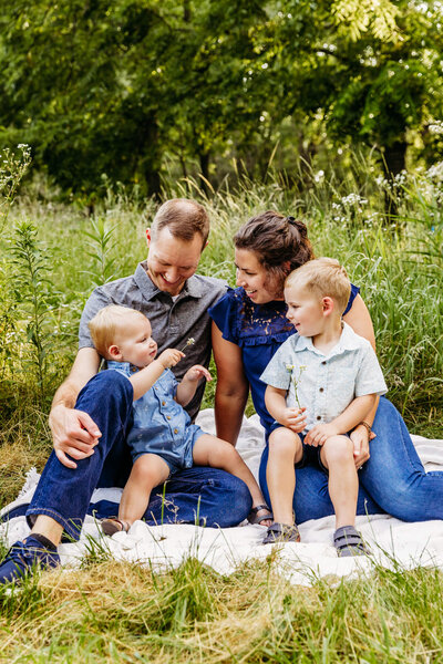 mother and father looking at their toddler son's as they play together while sitting on a blanket captured by Ashley Kalbus Photography