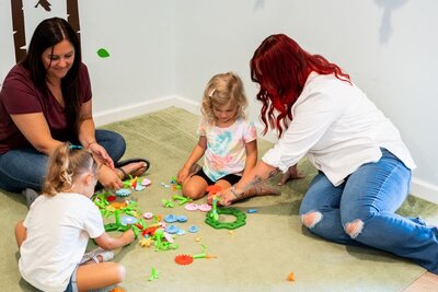 Ms. Brandi and Ms. Jo sitting with two students in a classroom at the Nest, a preschool in Surf City, North Carolina