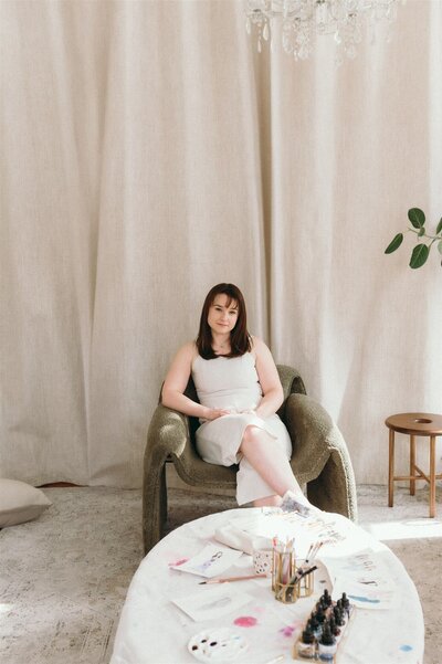 Custom watercolor artist Stephanie Anne seated in a Montreal studio, surrounded by her artwork
