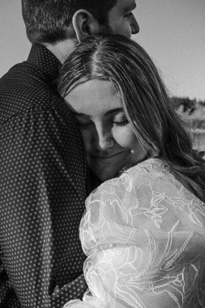 Two people embracing, one resting their head on the other's shoulder in a black and white photo.