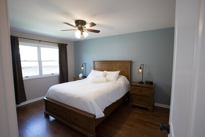 Wide shot of bedroom with blue walls and dark wood floors and furniture