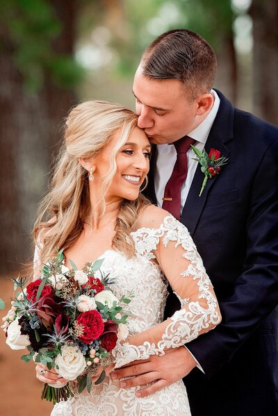 bride in lace dress and red bouquet with groom in navy