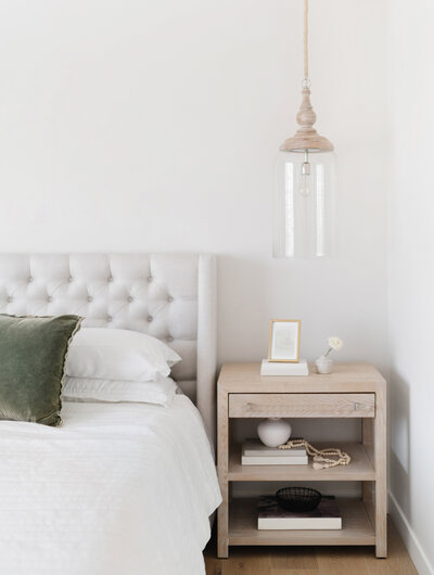 Bed with grey fabric headboard next to a light wooden nightstand and hanging light