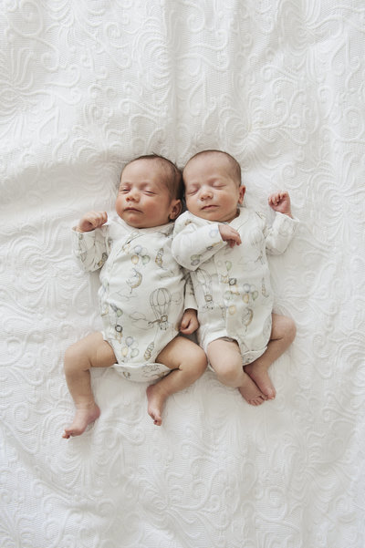 Newborn twin baby boys sleeping together. Babies wearing baby vests.