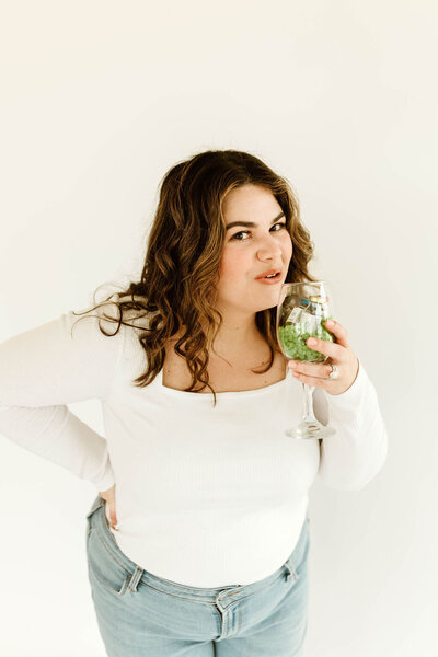 Macayla Hopper holding professional skincare tools used for facials and waxing services in a wine glass Hartselle AL