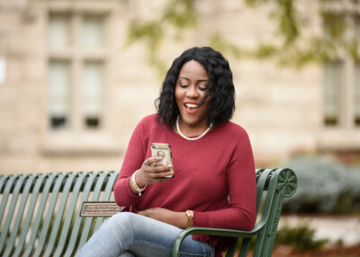 woman in red top sitting on park bench looking at her phone
