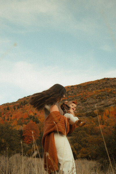 A mother twirling her baby  outdoors during fall in Park City, UT.