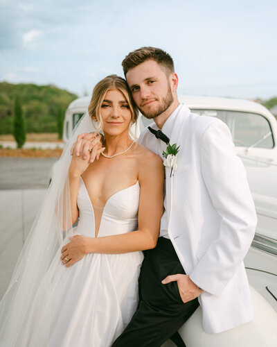 Bride and Groom embrace each other while leaning on their wedding getaway car.
