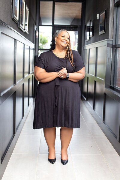 Kisha  standing at a table in black dress with book in her hand