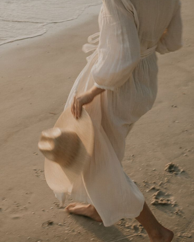 Woman walking barefoot on the beach in a flowing white dress, captured mid-step