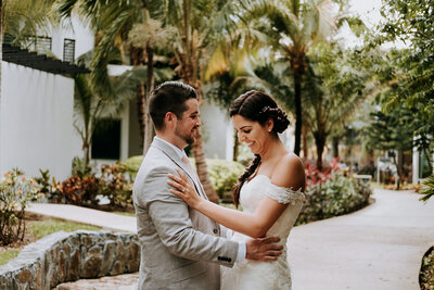 A couple stands close together on a landscaped path lined with trees and plants at The Fives in Playa del Carmen, elegantly dressed for their destination wedding day. Captured by Jennifer van Son, a talented destination wedding photographer, the moment exudes romance and sophistication.